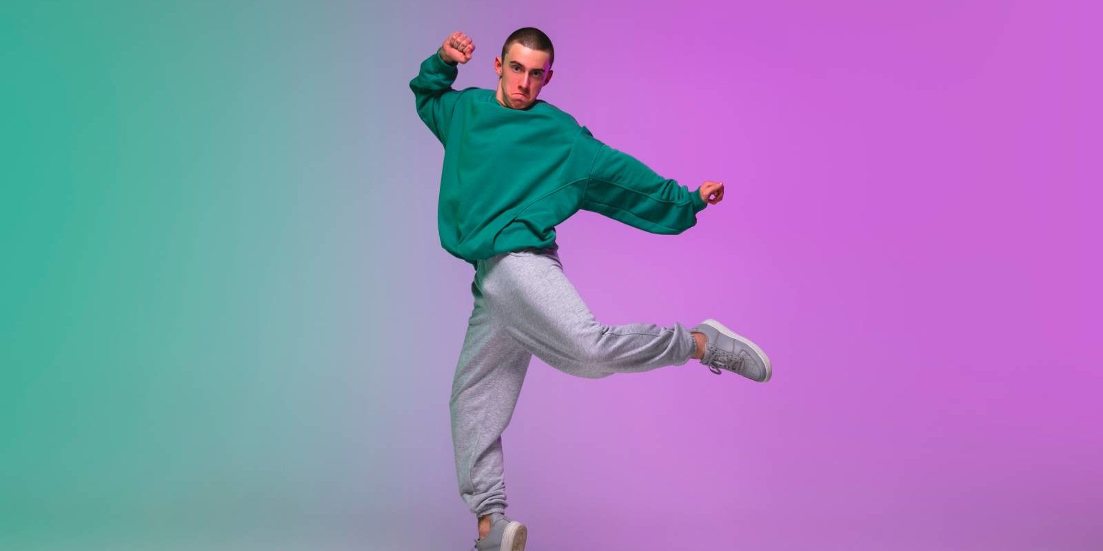 Boy dancing hip-hop in stylish clothes on gradient background at dance hall in neon light.