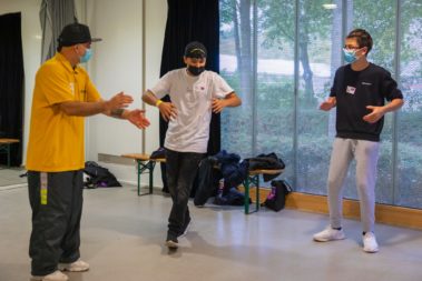 Links und rechts stehen zwei Personen die Klatschen, die Person in der Mitte tanzt