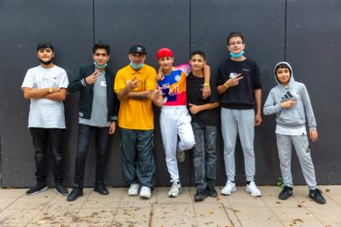 Sechs junge Menschen und ein älterer stehen vor einer Wand und posieren für das Bild.