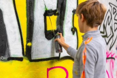 Ein junger Mensch mit kurzen Haaren sprüht mit grün an eine Wand